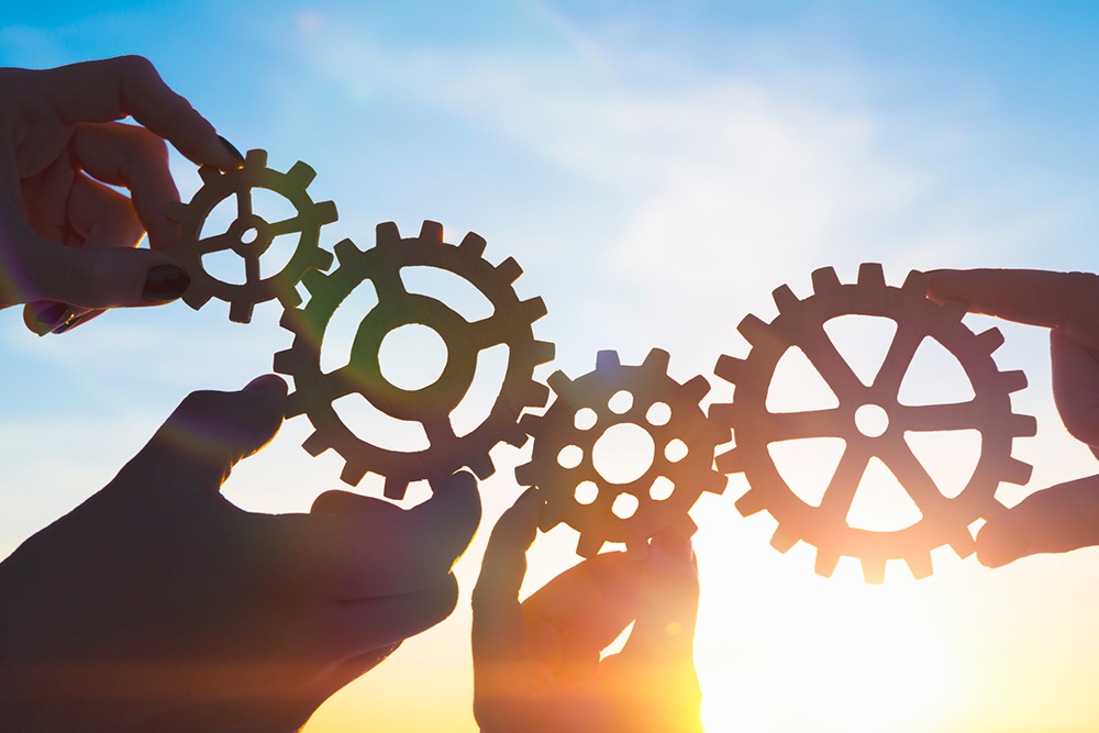 Teamwork and collaboration concept with hands connecting gears at sunset.