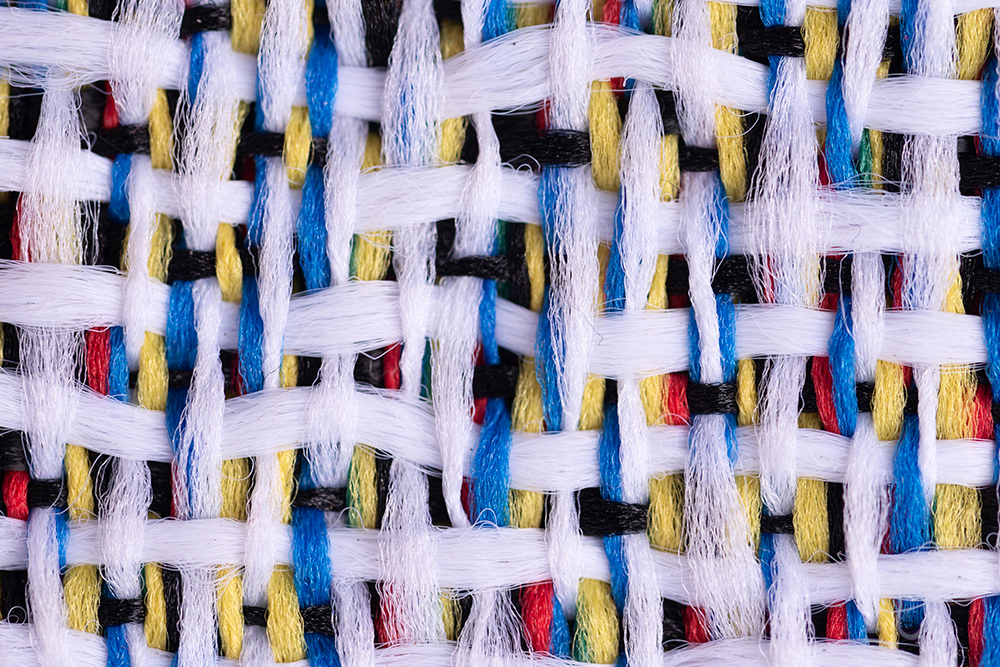 Close-up top view of colorful woven fabric texture with red, yellow, blue, black, and white threads